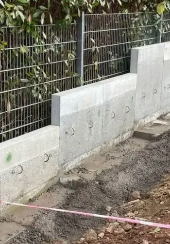 Moderne Abgrenzung aus Betonplatten kombiniert mit einem stabilen Stahlzaun.