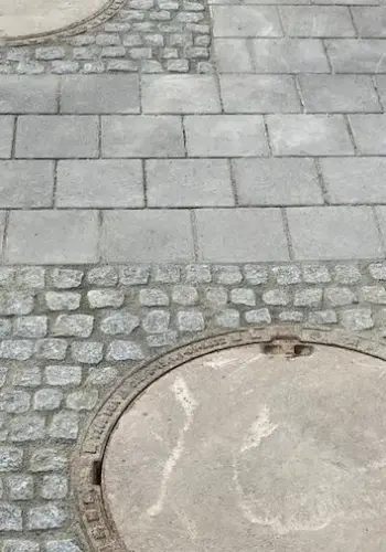 Professionell eingefasster Schachtzugang für einen Erdtank, umrandet mit Pflastersteinen.